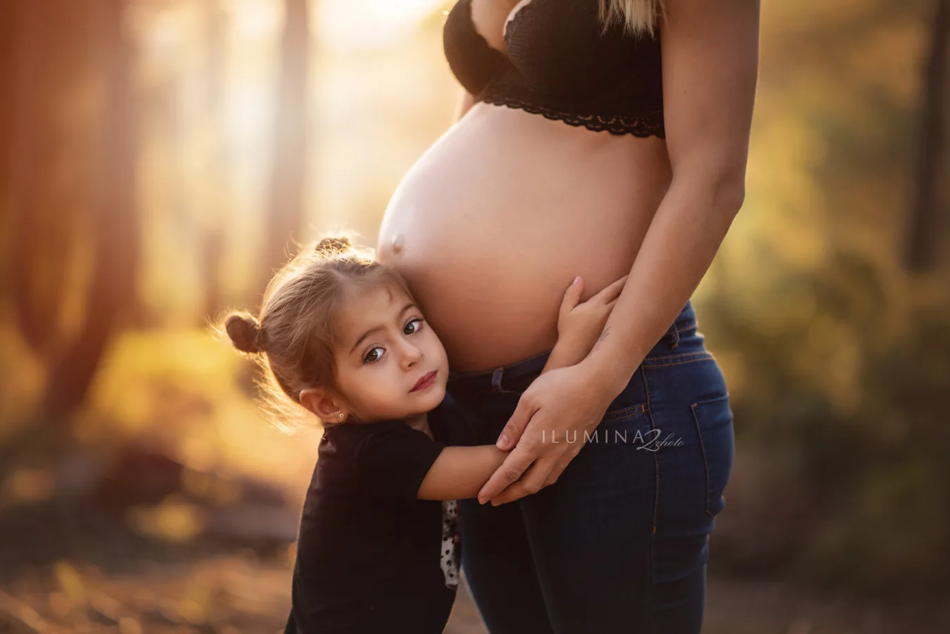 Niña abrazando la barriga de su madre en un book premamá familiar en Barcelona