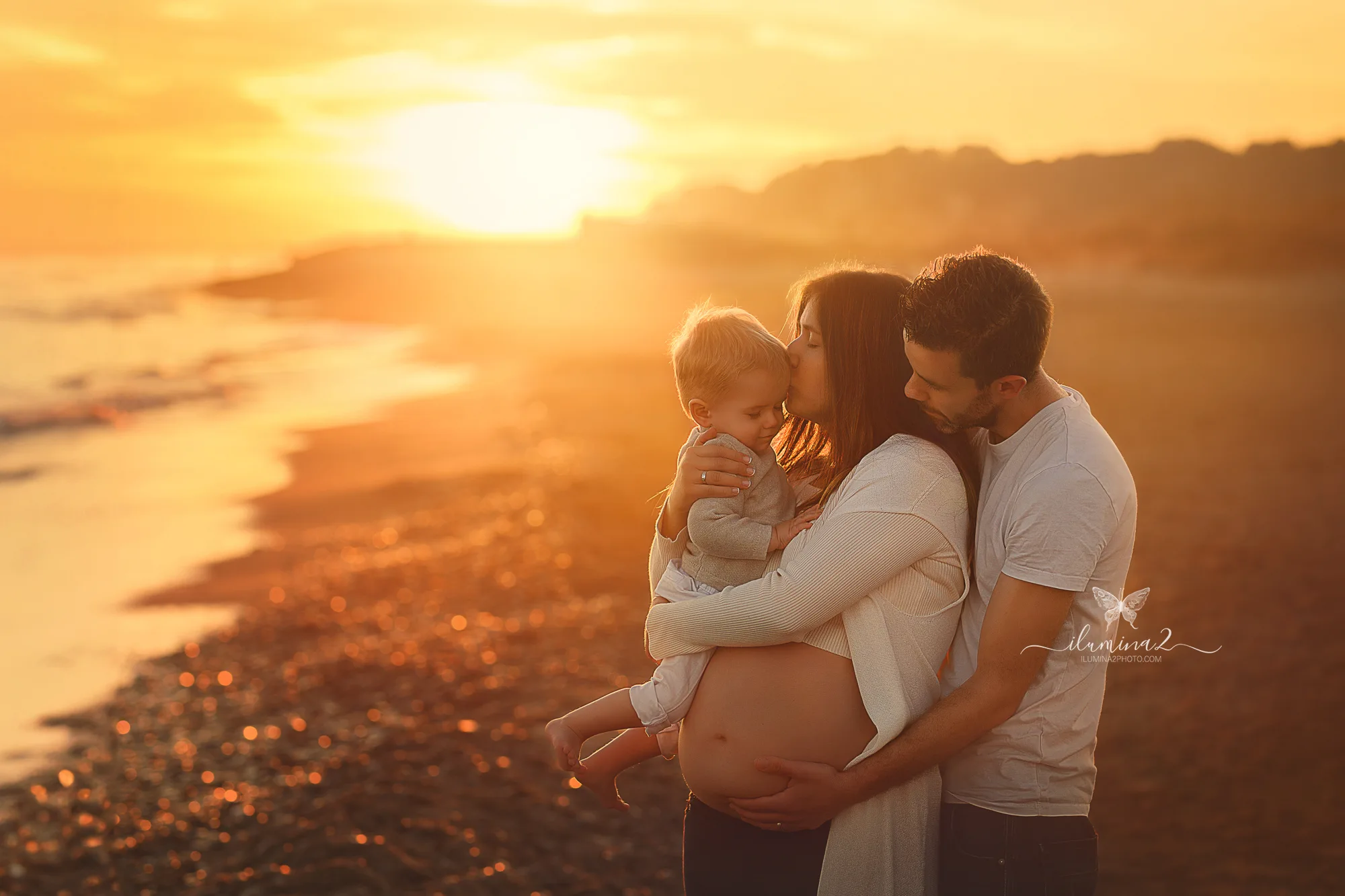 Pareja con su hija en un reportaje de embarazo en la playa al atardecer en Barcelona