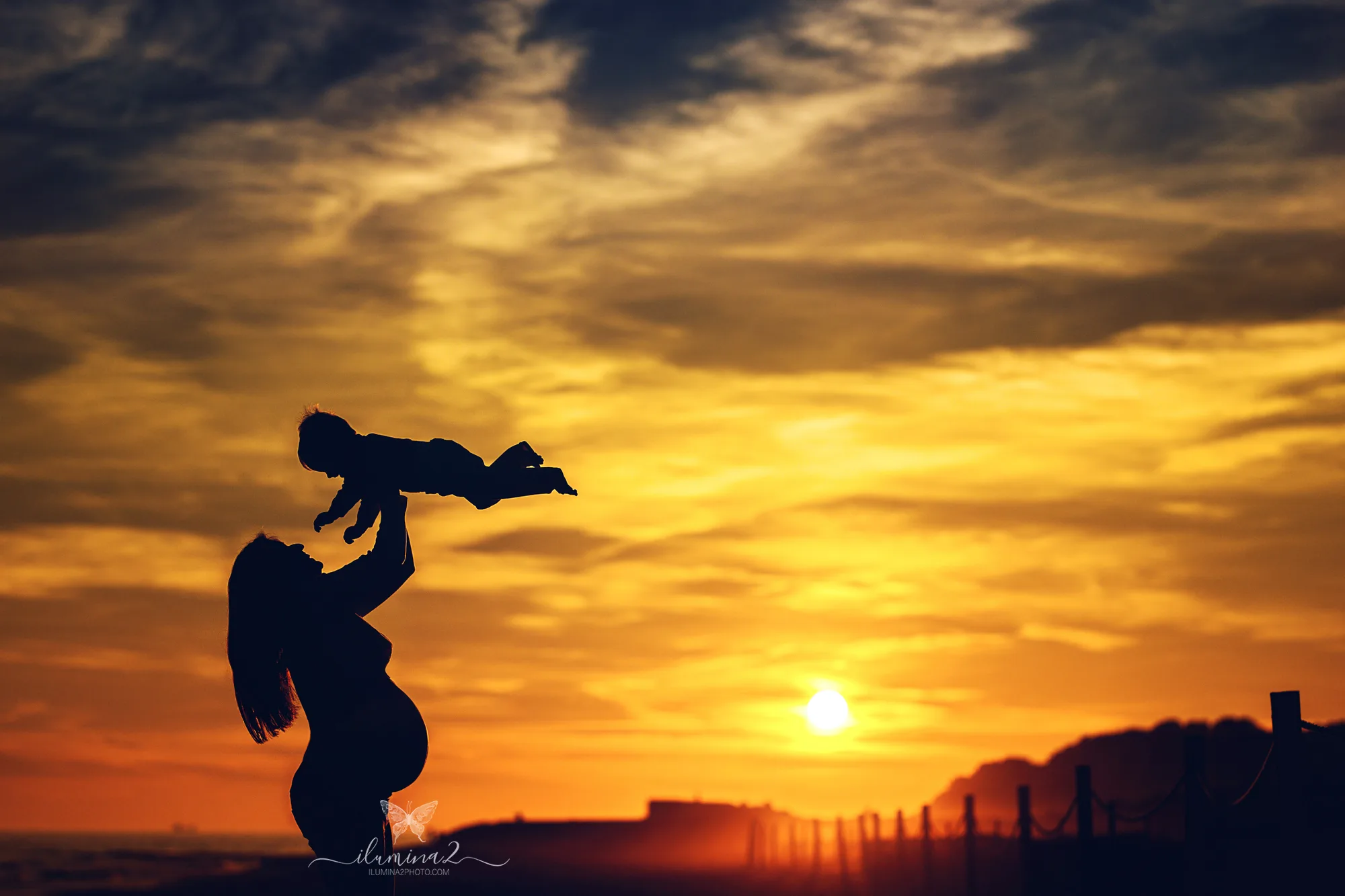 Silueta de una mamá embarazada jugando con su hija durante una sesión de embarazo al atardecer en Barcelona