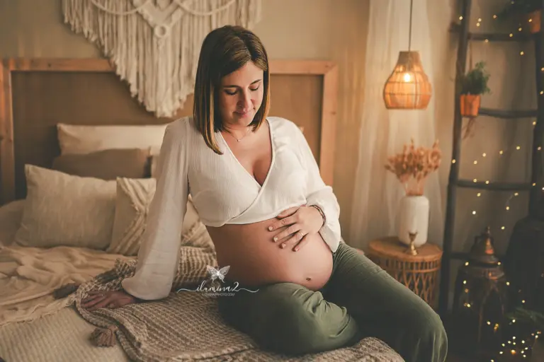 Mamá embarazada durante una sesión de fotos en estudio iluminada por luz natural de ventana