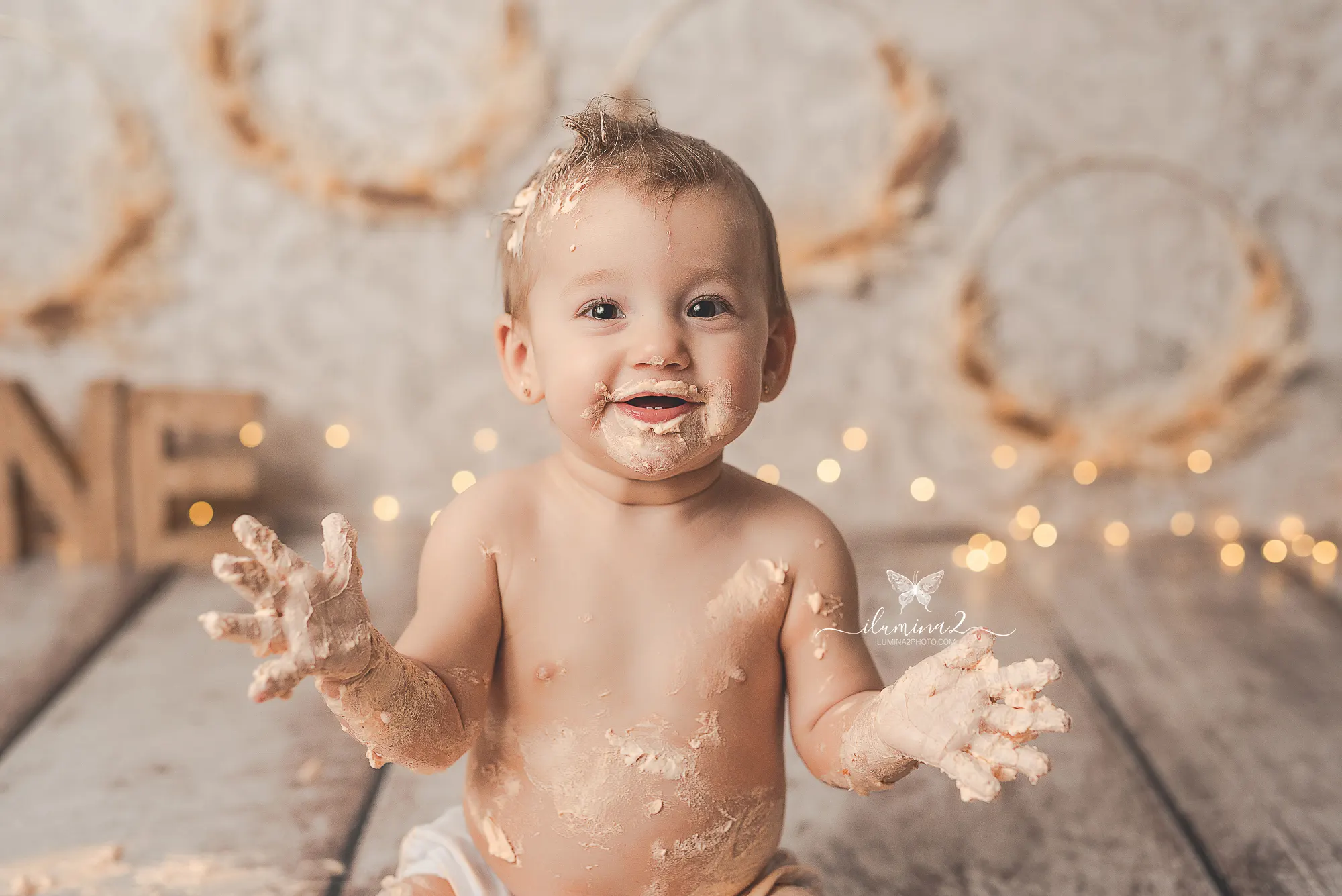 Bebé mostrando sus manos llenas de nata durante su sesión de fotos de primer cumpleaños Cake Smash