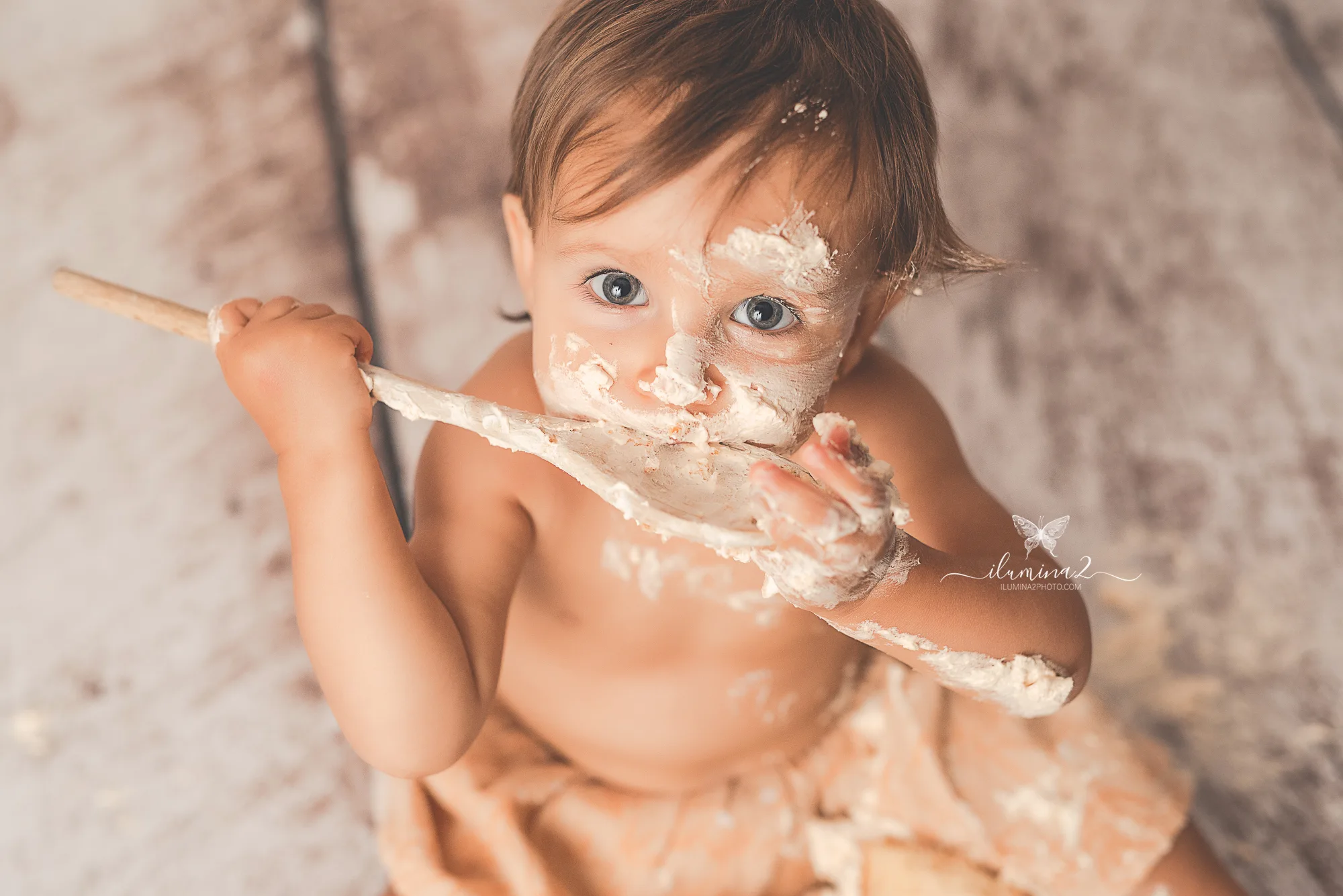 Bebé mirando a cámara mientras prueba la crema de su pastel en un reportaje Smash Cake de primer cumpleaños
