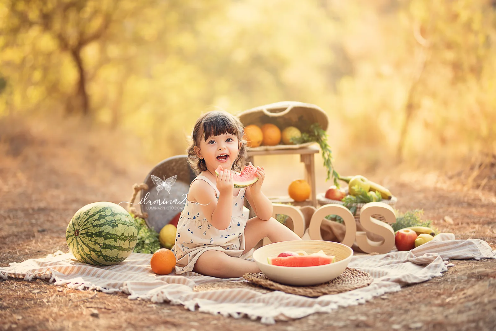 Bebé comiendo sandía rodeada de fruta en una sesión Smash Cake con fruta en exterior