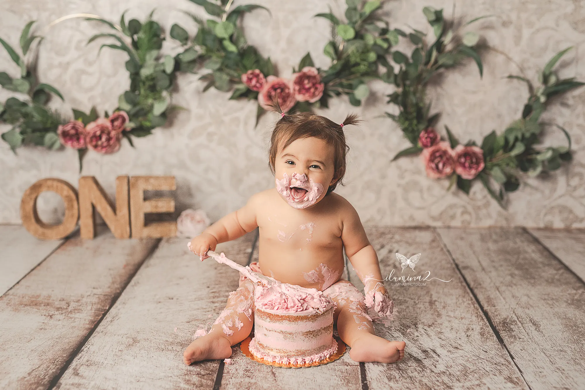 Bebé con la cara manchada de crema rosa junto a su pastel en una sesión Smash Cake en Barcelona