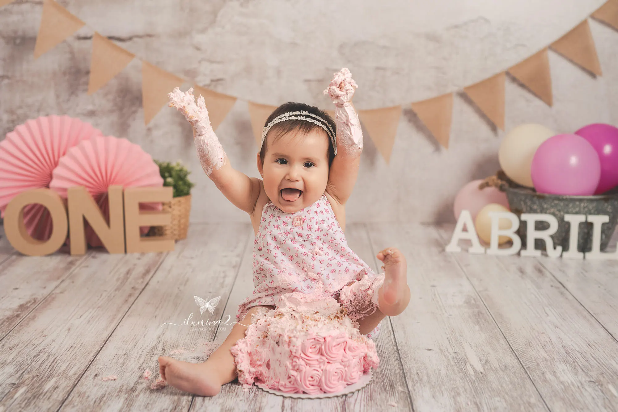 Bebé con vestido rosa riendo con los brazos en alto durante su sesión Smash Cake