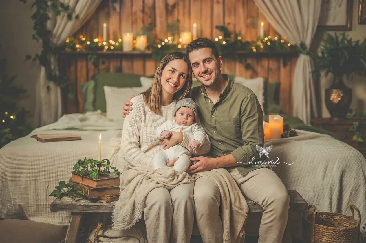 Sesiones de fotos de Navidad Ilumina2 Photo Retrato navideño de una familia con mamá, papá y bebé mirando a cámara, ideal para una postal de Navidad personalizada