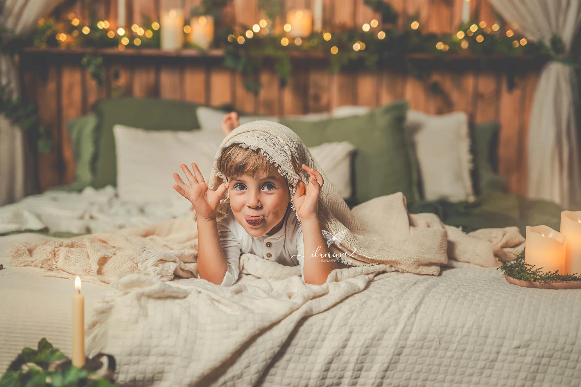 Sesiones de fotos de Navidad Ilumina2 Photo Niño escondido sobre la cama del decorado en su sesión de fotos de Navidad para niños